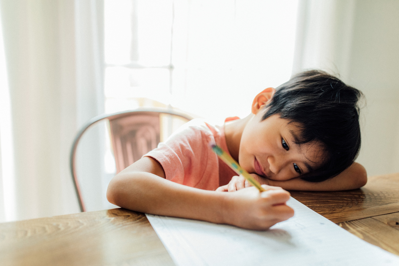 Kid writing on paper with a pencil at home
